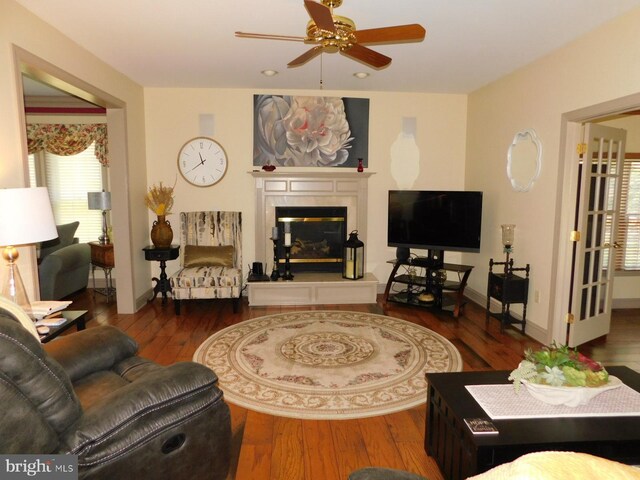 living area with baseboards, a tiled fireplace, wood finished floors, and ceiling fan