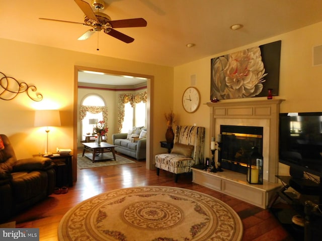 living area featuring wood finished floors, a fireplace, ceiling fan, and crown molding