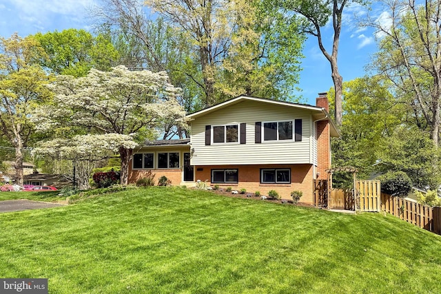 tri-level home with fence, a chimney, brick siding, and a front yard