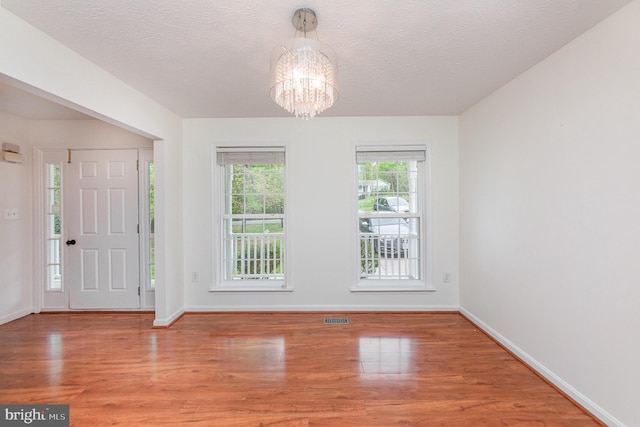 entryway featuring visible vents, baseboards, light wood-style flooring, a textured ceiling, and a notable chandelier