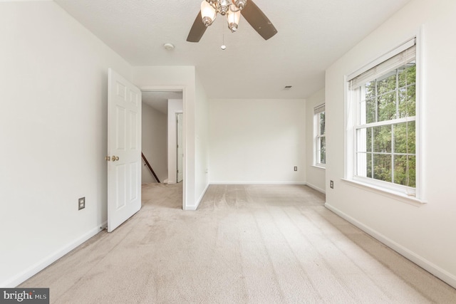 spare room with light colored carpet, baseboards, and a ceiling fan