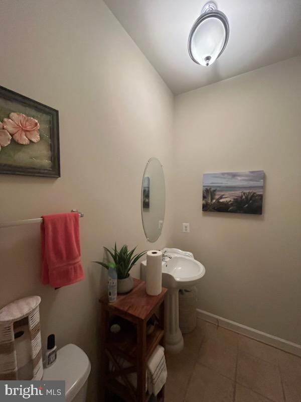 half bathroom featuring tile patterned flooring, baseboards, a sink, and toilet