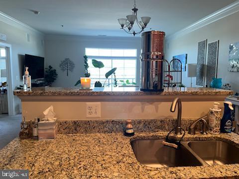 kitchen with a chandelier, ornamental molding, light stone countertops, and a sink