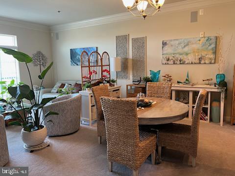 dining space featuring carpet floors, crown molding, and a notable chandelier