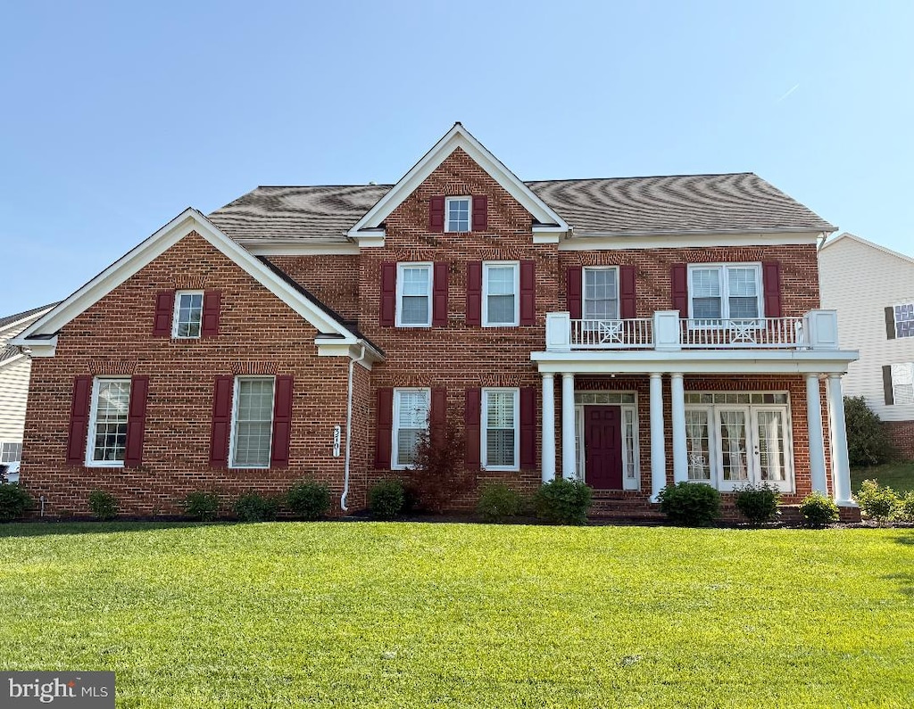 view of front facade featuring brick siding, a shingled roof, a balcony, and a front yard