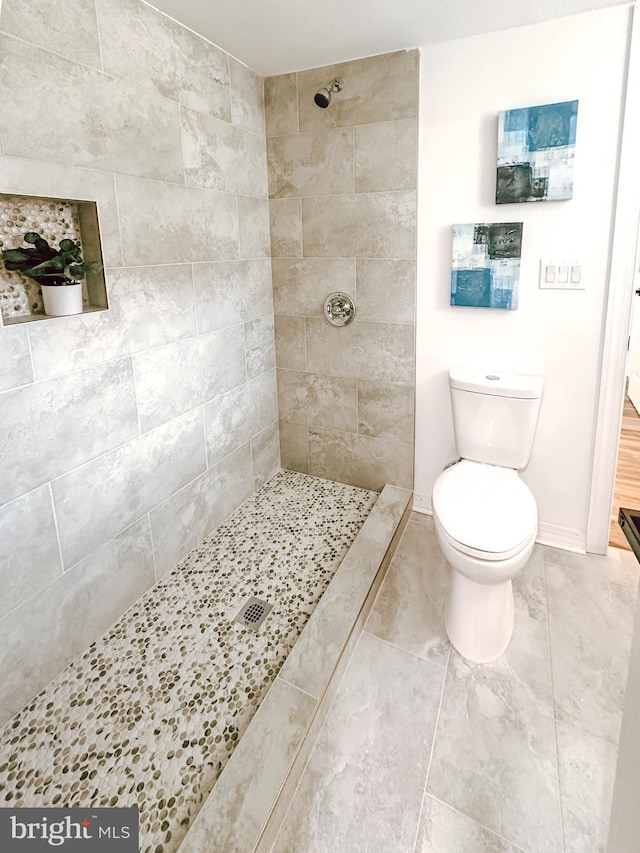 full bath featuring a tile shower, toilet, and baseboards