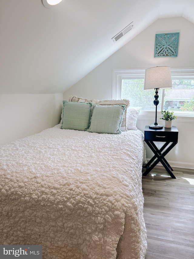 bedroom with wood finished floors, visible vents, vaulted ceiling, and multiple windows