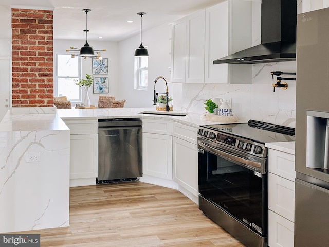kitchen with a peninsula, stainless steel appliances, a sink, white cabinetry, and wall chimney exhaust hood
