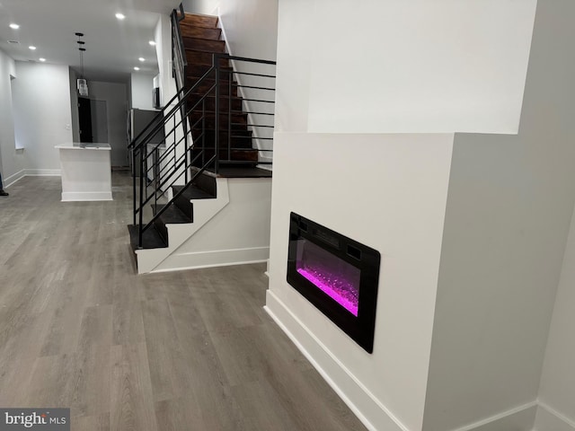 staircase with a glass covered fireplace, baseboards, recessed lighting, and wood finished floors