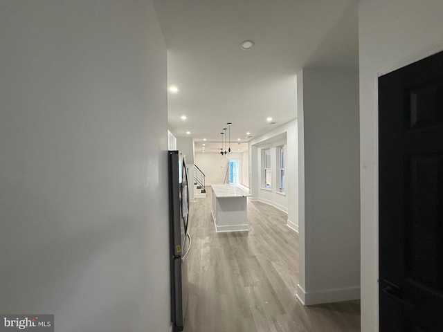 corridor featuring recessed lighting, baseboards, a notable chandelier, and light wood-style flooring
