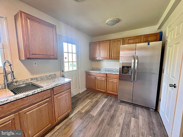 kitchen with dark wood-type flooring, stainless steel fridge, brown cabinetry, and a sink