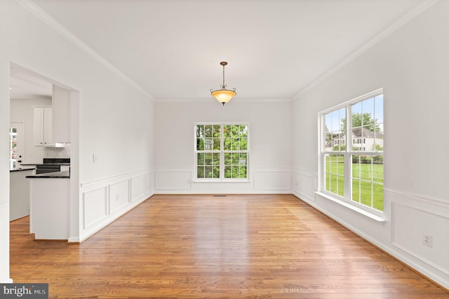 unfurnished dining area with healthy amount of natural light, crown molding, light wood-style flooring, and a wainscoted wall