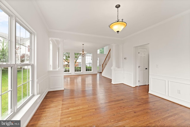 empty room featuring a chandelier, ornamental molding, light wood-type flooring, ornate columns, and stairs