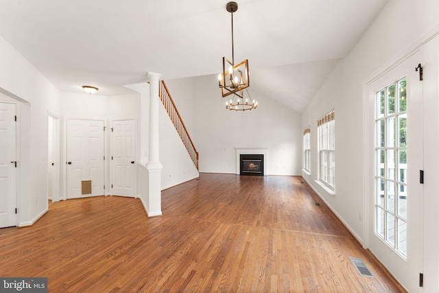 unfurnished living room featuring wood finished floors, a lit fireplace, stairs, a chandelier, and lofted ceiling