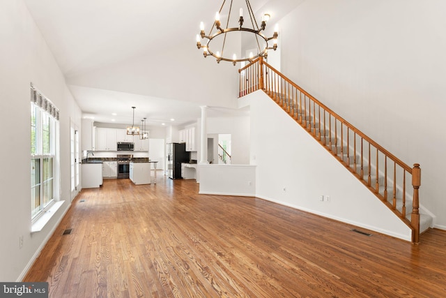 unfurnished living room with a chandelier, high vaulted ceiling, light wood finished floors, stairs, and baseboards