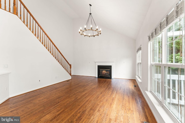 unfurnished living room with high vaulted ceiling, wood finished floors, a chandelier, stairway, and a fireplace with flush hearth