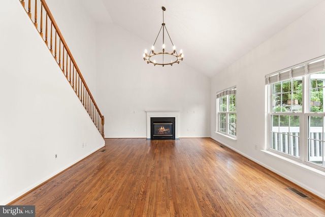 unfurnished living room with a chandelier, wood finished floors, high vaulted ceiling, a fireplace with flush hearth, and baseboards