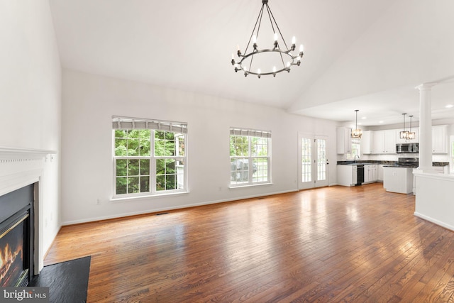 unfurnished living room featuring a chandelier, light wood finished floors, a fireplace with flush hearth, high vaulted ceiling, and baseboards
