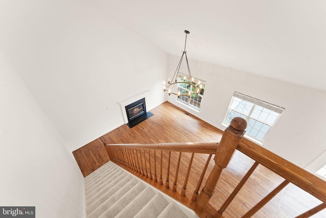stairway featuring high vaulted ceiling, a chandelier, a fireplace with flush hearth, and wood finished floors