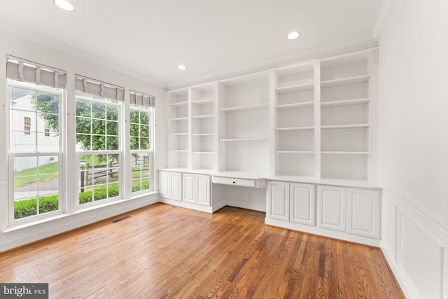 unfurnished office featuring crown molding, built in desk, light wood-type flooring, recessed lighting, and built in shelves