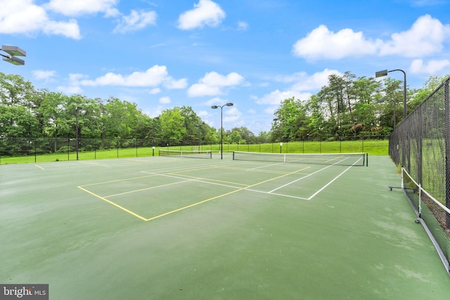 view of tennis court with fence, community basketball court, and view of scattered trees