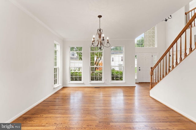 unfurnished dining area with stairs, wood finished floors, a chandelier, ornamental molding, and baseboards