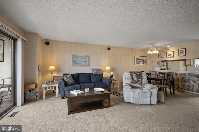 living area featuring ceiling fan, carpet flooring, a textured ceiling, and visible vents