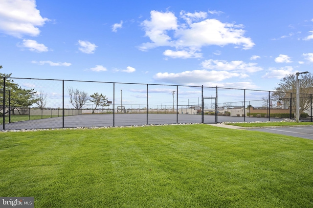 view of tennis court featuring fence and a yard