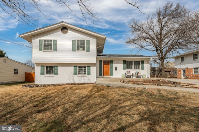 tri-level home featuring brick siding, a front lawn, and fence