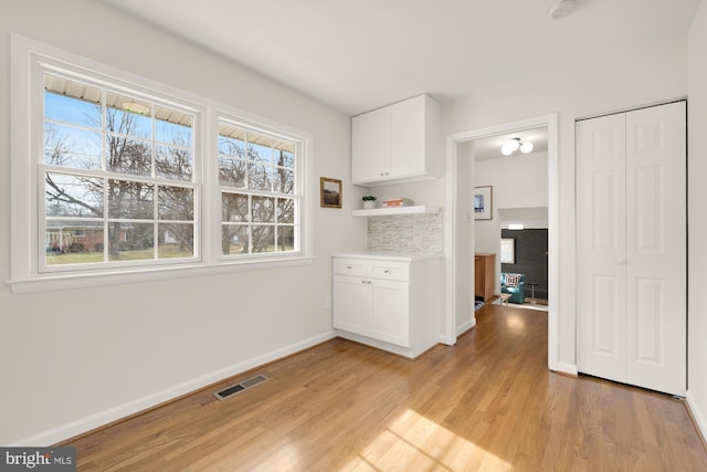 interior space featuring baseboards, light wood finished floors, a healthy amount of sunlight, and visible vents