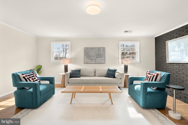 living area with brick wall, visible vents, ornamental molding, and wood finished floors