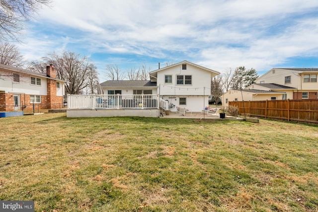 rear view of property featuring a lawn, a patio area, fence, and a wooden deck