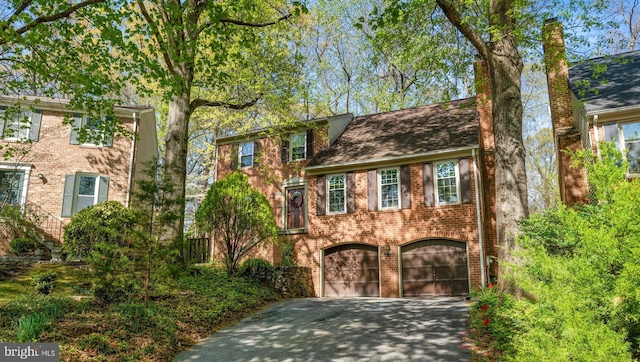 colonial home featuring asphalt driveway, an attached garage, brick siding, and a chimney