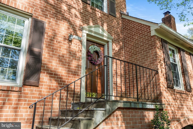view of exterior entry with brick siding and a chimney