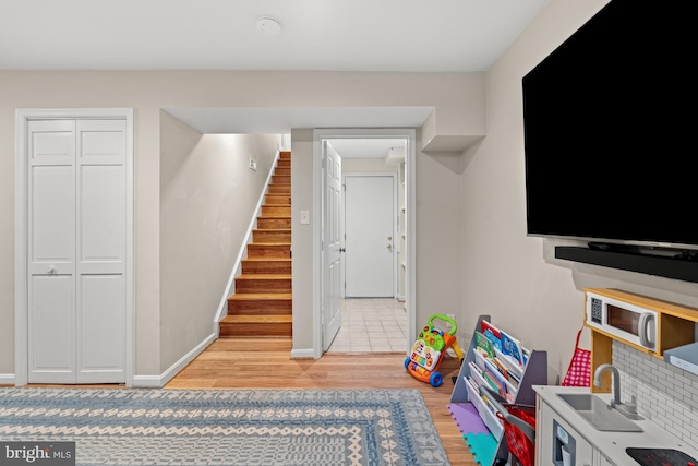 rec room featuring light wood-type flooring, a sink, and baseboards