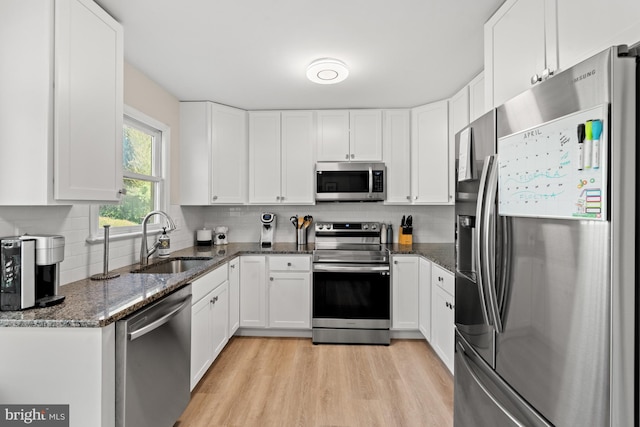 kitchen with appliances with stainless steel finishes, a sink, light wood-style floors, white cabinets, and decorative backsplash