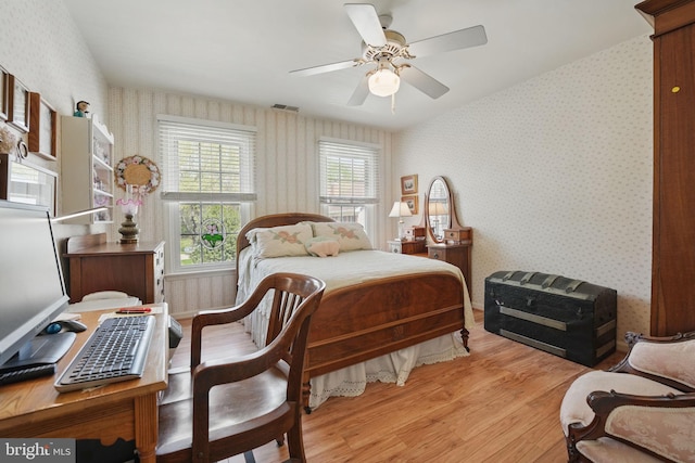 bedroom with a ceiling fan, visible vents, light wood-style floors, and wallpapered walls