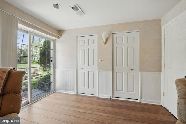 interior space with wood finished floors, access to exterior, a wainscoted wall, and visible vents