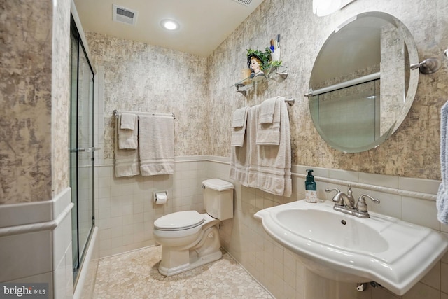 bathroom featuring a sink, toilet, tile walls, visible vents, and an enclosed shower