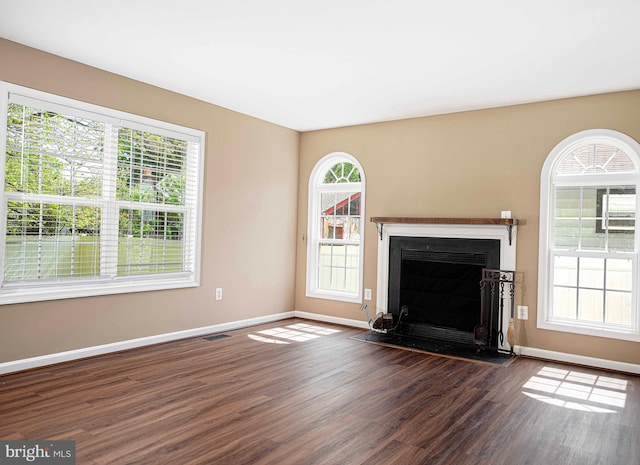unfurnished living room featuring baseboards, dark wood finished floors, plenty of natural light, and visible vents