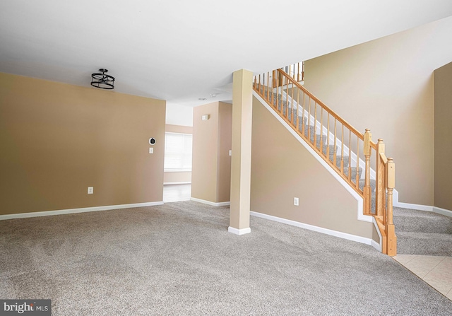 unfurnished living room with baseboards, carpet, and stairs