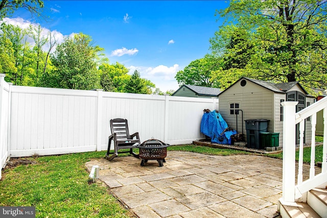 view of patio featuring a storage shed, an outdoor structure, a fire pit, and a fenced backyard
