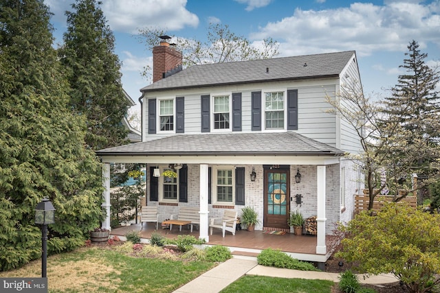 farmhouse-style home featuring a chimney, a front lawn, roof with shingles, and covered porch