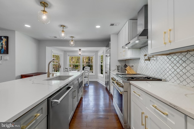 kitchen featuring wall chimney range hood, premium appliances, a sink, dark wood-style flooring, and visible vents