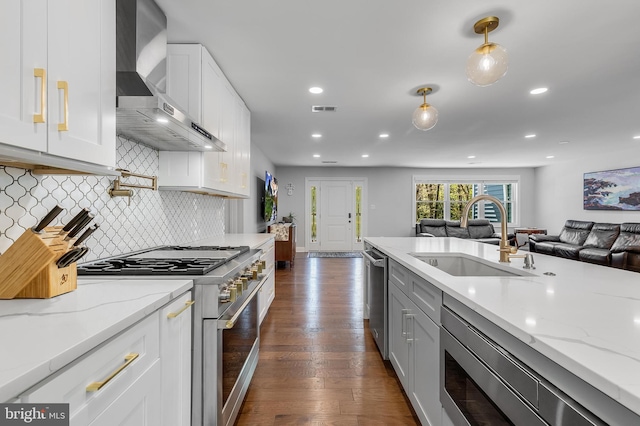 kitchen featuring dark wood-style floors, stainless steel appliances, visible vents, a sink, and wall chimney exhaust hood