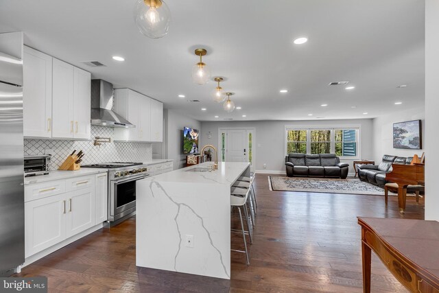kitchen featuring wall chimney exhaust hood, high end stainless steel range oven, white cabinetry, and a sink