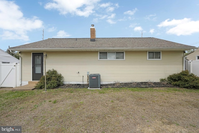 rear view of house featuring central AC unit, fence, and a yard