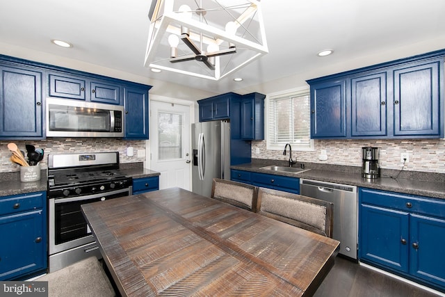 kitchen featuring blue cabinets, dark countertops, stainless steel appliances, and a sink