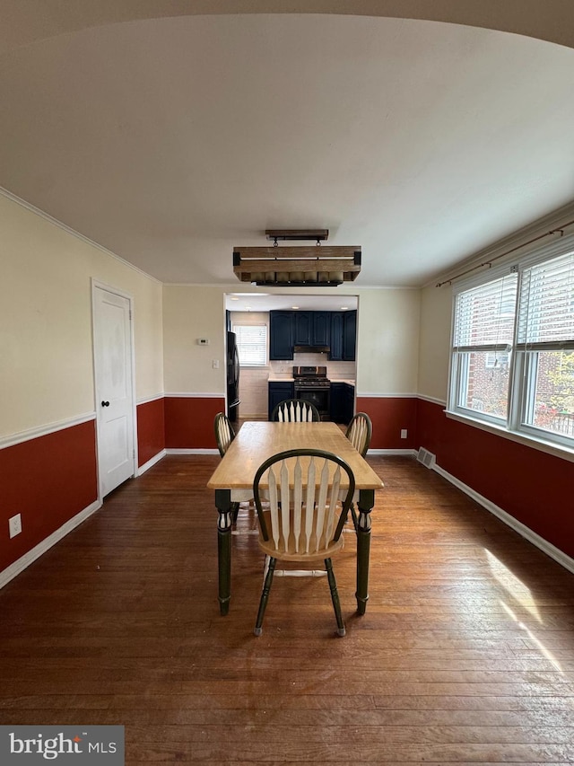 dining room featuring a healthy amount of sunlight, a wainscoted wall, visible vents, and dark wood-style floors