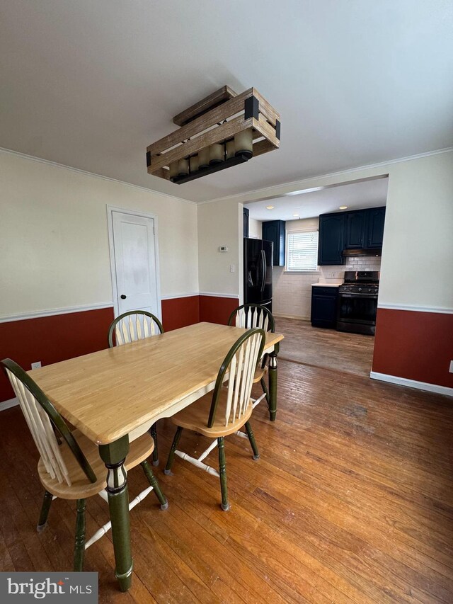 dining area featuring crown molding, wood finished floors, and a wainscoted wall